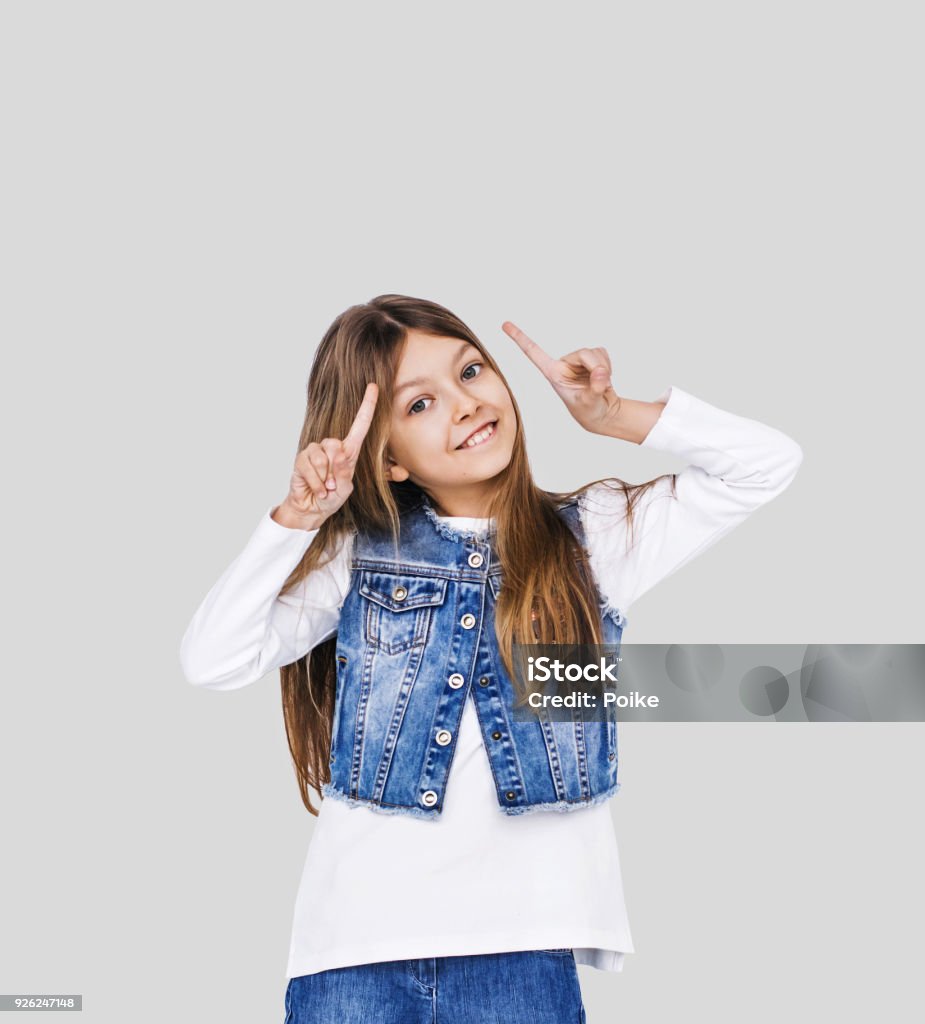 Cute little girl pointing up Smiling elementary student girl pointing on empty space. Isolated on grey background Humor Stock Photo