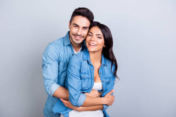 Portrait of cheerful lovely cute couple with beaming smiles hugging and looking at camera over grey background Portrait of cheerful lovely cute couple with beaming smiles hugging and looking at camera over grey background boyfriend stock pictures, royalty-free photos & images