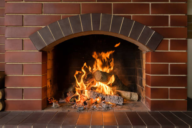 A brick fireplace in which a fire burns Firewood and hot coals burn in a brick fireplace with bright fire fireplace stock pictures, royalty-free photos & images