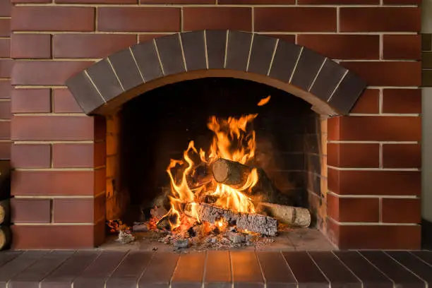 Firewood and hot coals burn in a brick fireplace with bright fire