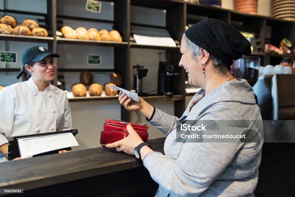 Customer service in a small local bakery shop. Customer service in a small local bakery shop. Owner interacting with clients at the cash register. Horizontal waist up indoors shot with copy space. This was taken in Montreal, Canada. Paper Currency Stock Photo