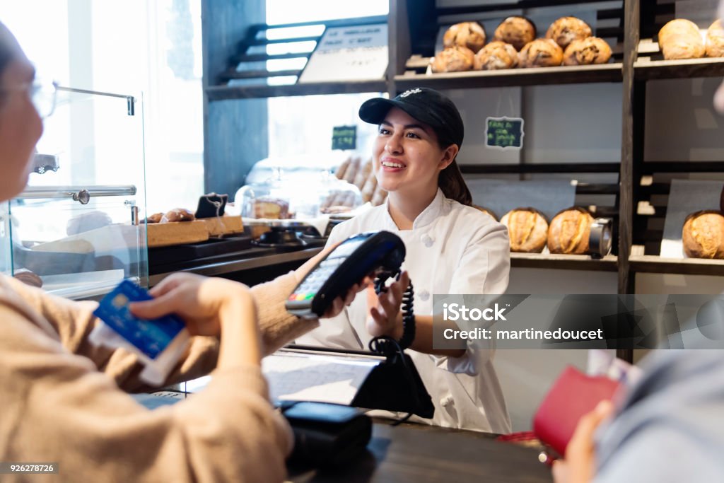 Customer service in a small local bakery shop. Customer service in a small local bakery shop. Owner interacting with clients at the cash register. Horizontal waist up indoors shot with copy space. This was taken in Montreal, Canada. Small Business Stock Photo