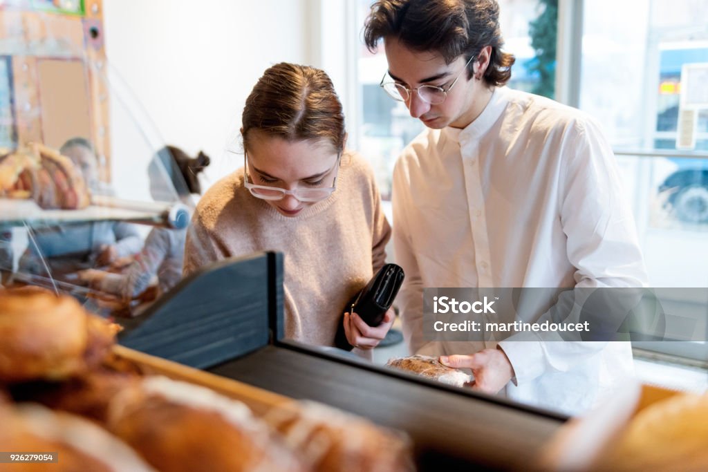 Customer choosing something to eat in a small local bakery shop. Customer choosing something to eat in a small local bakery shop. Focus on faces of clients. Pastries and cookies in the foreground. Horizontal waist up indoors shot with copy space. This was taken in Montreal, Canada. 20-24 Years Stock Photo