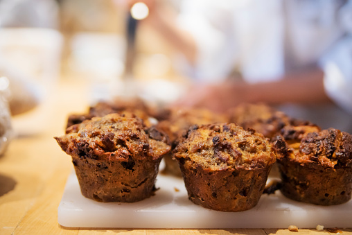 Close-up on muffins in small local bakery shop. Small detail of hands of the baker in the blurred background. Horizontal indoors shot with copy space. This was taken in Montreal, Canada.