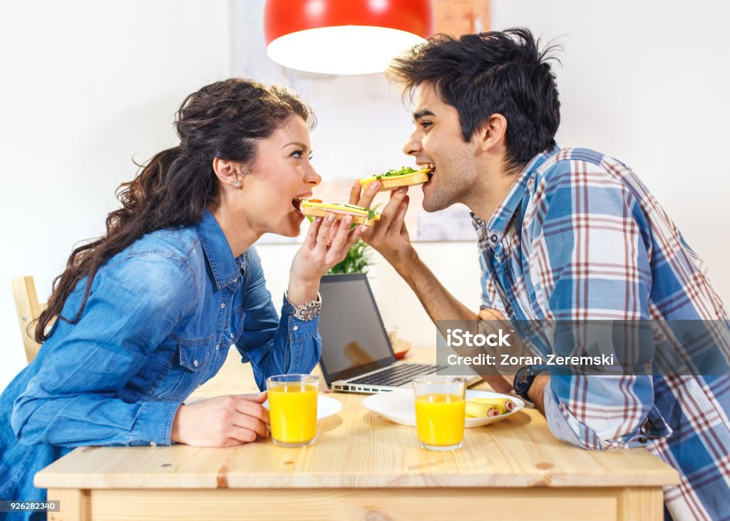 Young couple sitting by table and eating breakfast early in the morning together. 20-24 Years Stock Photo