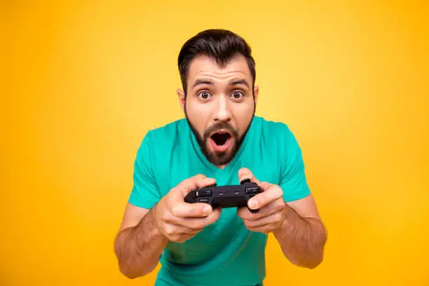 Photo of I am number one in playing games! Close up portrait of funny joyful cheerful happy guy, he is rejoicing his victory with gamepad in hands, isolated on bright yellow background