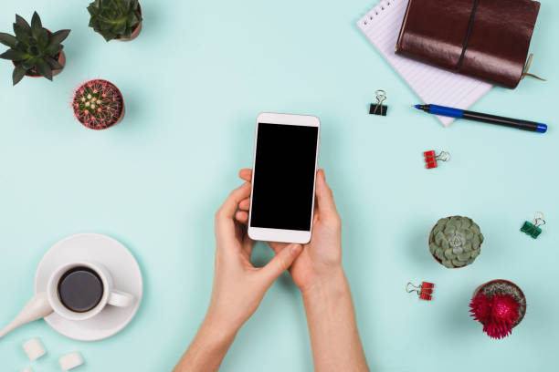 istock Business flatlay arrangement with woman's hands holding smartphone with black copyspace and other stationary and office accessories. Mint background. Business mockups 926295950