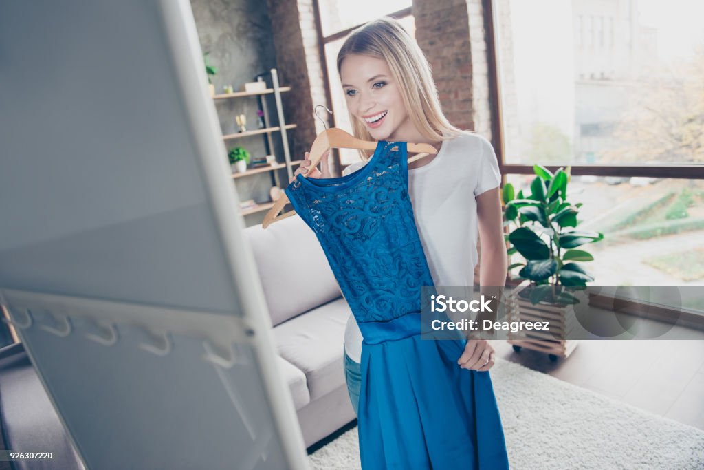 I want to wear this elegant beautiful blue dress! Pretty smiling happy excited joyful delightful blond is trying on new dress in front of a mirror I want to wear this elegant beautiful blue dress! Pretty smiling happy excited joyful delightful blonde is trying on new dress in front of a mirror Dress Stock Photo