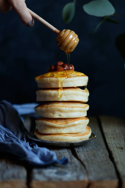 istock Hand is holding a honey dipper with pouring honey above a stack of pancakes with nuts on a wooden table. Still life in a rustic style. 926307898