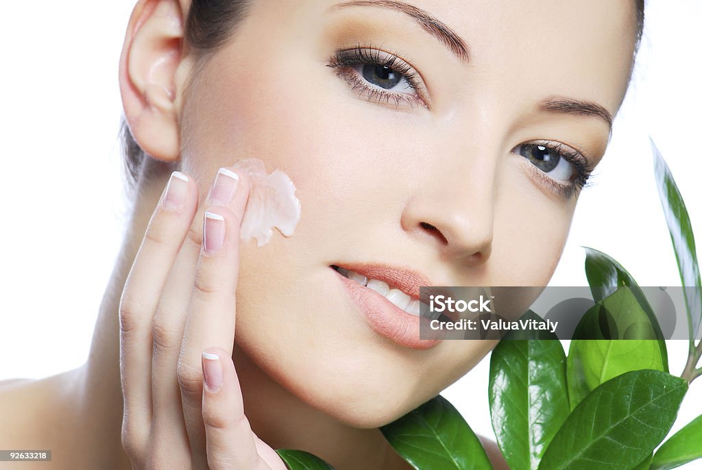 Beauty Woman applying moisturizer cream on face. Close-up fresh woman face. Getting Dressed Stock Photo