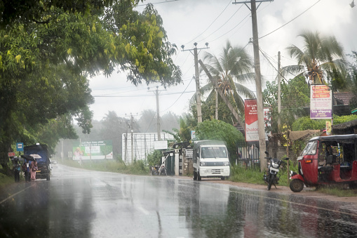 Gokarella, Sri Lanka - December 3, 2017: Typical Sri Lankan road in heavy rain, people with umbrellas, billboards and a truck