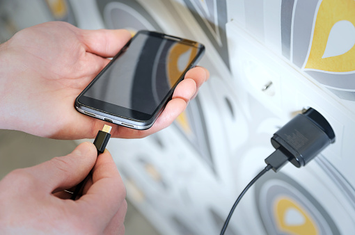 A man is inserting a power cord into the mini USB for charging the smartphone.