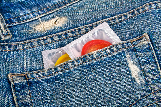 préservatifs colorés dans une poche de jeans bleu - sex condom jeans horizontal photos et images de collection