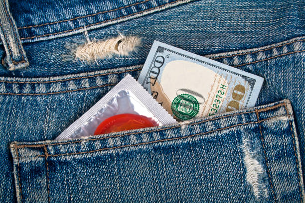 préservatif rouge et cent dollars dans une poche de jeans bleu - sex condom jeans horizontal photos et images de collection