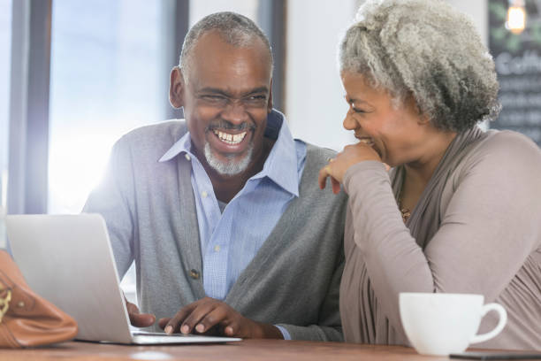 istock Senior couple laugh while looking at laptop in cafe 926363028