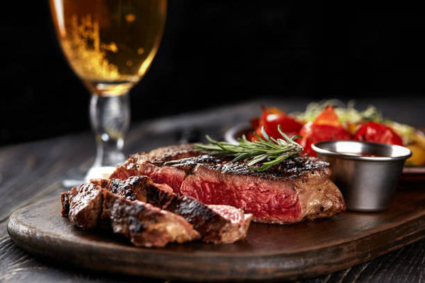 Juicy steak medium rare beef with spices on wooden board on table Juicy steak medium rare beef with spices on wooden board on table. dry aged. Served with potatoes, beer, and tomato sauce. Still life steak stock pictures, royalty-free photos & images