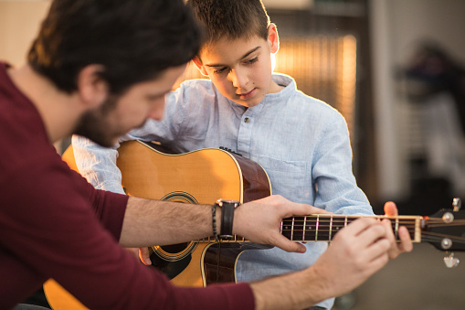 Young man teaching a boy to play the guitar