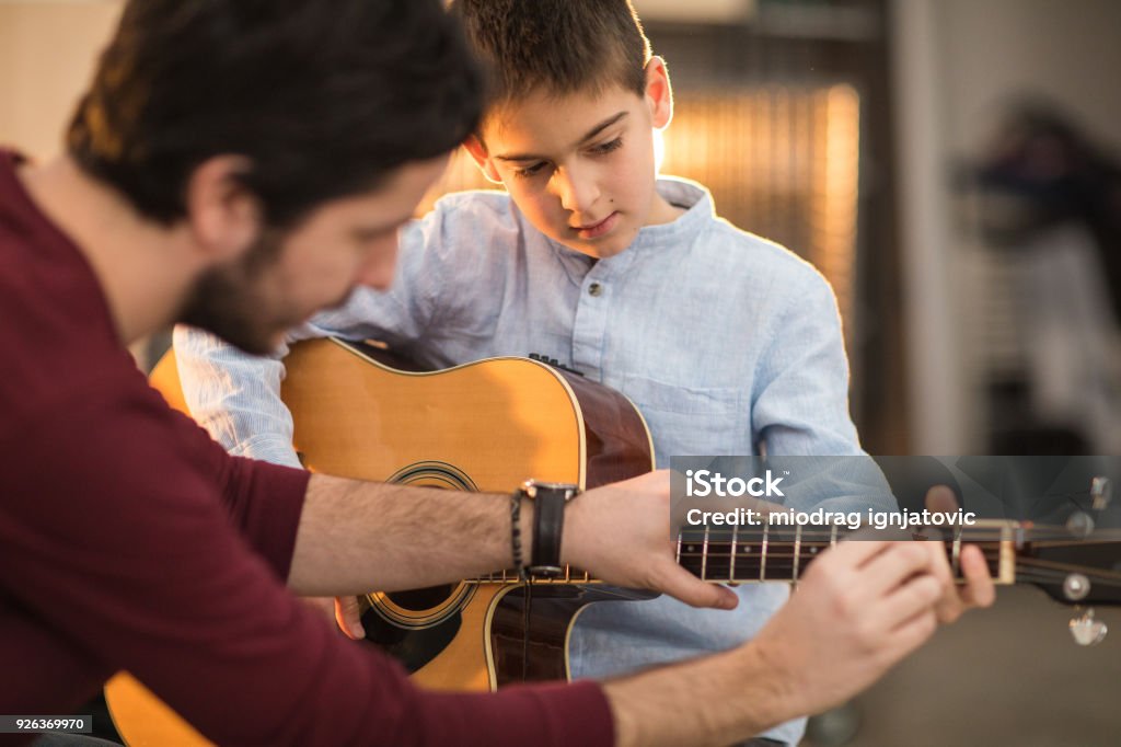 Playing the guitar with my brother Young man teaching a boy to play the guitar Learning Stock Photo