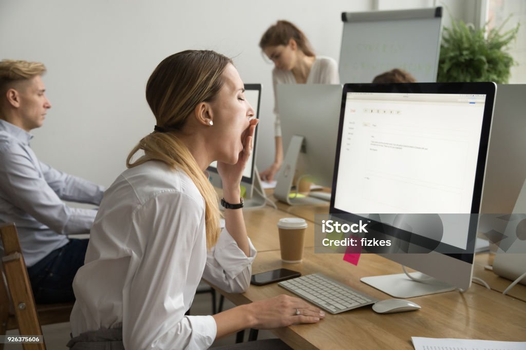 Tired businesswoman yawning working on computer sitting at office desk Tired businesswoman yawning working on computer sitting at desk with colleagues, sleepy employee gaping suffering from lack of sleep, feeling bored or chronic fatigue in office concept, side view Sleeping Stock Photo