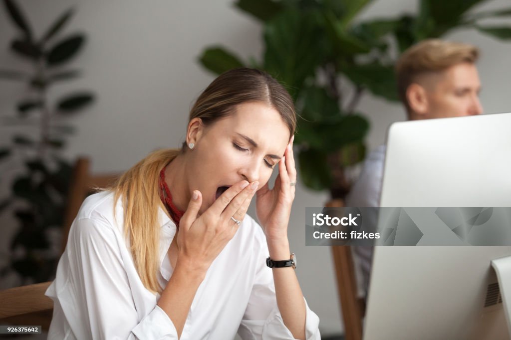 Bored tired businesswoman yawning at workplace feeling lack of sleep Bored businesswoman yawning at workplace feeling no motivation or lack of sleep tired of boring office routine, exhausted restless employee gaping suffering from chronic fatigue or overwork concept Tired Stock Photo