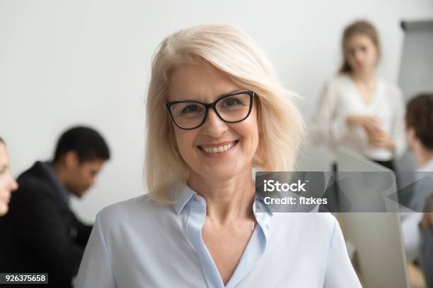 Smiling Senior Businesswoman Wearing Glasses Portrait With Businesspeople At Background Stock Photo - Download Image Now