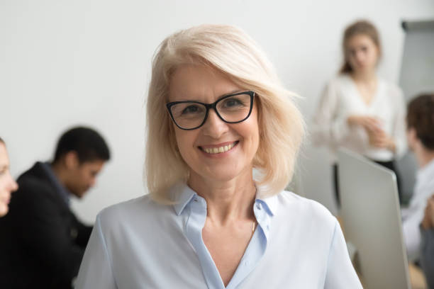 smiling senior businesswoman wearing glasses portrait with businesspeople at background - women professor mature adult human face imagens e fotografias de stock