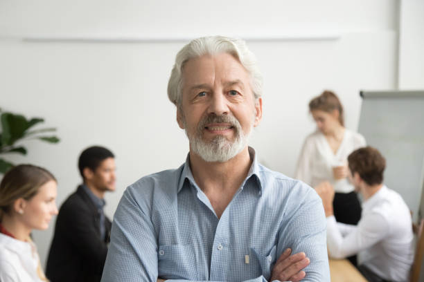 confident senior businessman leader looking at camera, team at background - old human face men ceo imagens e fotografias de stock