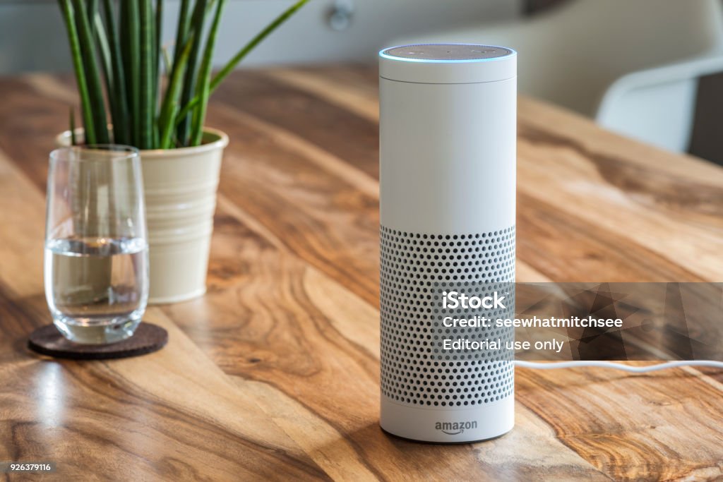 Amazon Echo, the voice recognition streaming device from Amazon MUENSTER - JANUARY 27, 2018: White Amazon Echo Plus, Alexa Voice Service activated recognition system photographed on wooden table in living room, Packshot showing Amazon Logo Amazon Echo Stock Photo