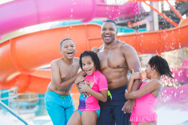 Family with three children at water park An African-American father with his mixed race African-American and Hispanic children, a 12 year old son and two 7 year old daughters at a water park. male swimsuit standing arm around stock pictures, royalty-free photos & images