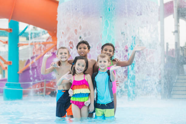 Multi-ethnic children at water park A multi-ethnic group of children, 6 to 8 years old, having fun at a water park. They are standing together in front of falling water, smiling at the camera. male swimsuit standing arm around stock pictures, royalty-free photos & images