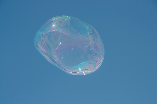 A solitary bubble floating in the air against a clear blue sky.