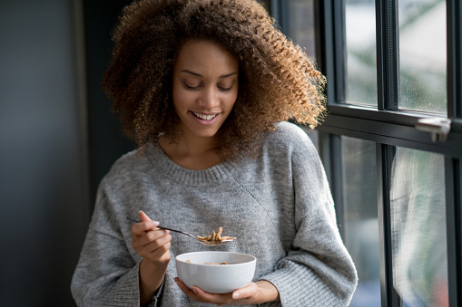 Portrait of a woman at home eating a bowl of cereals for breakfast - healthy eating concepts