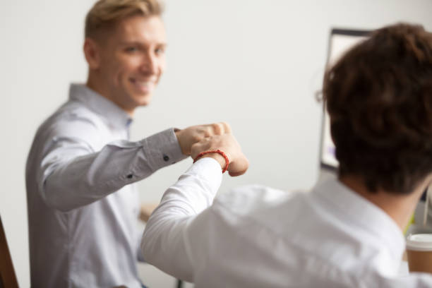 Smiling male colleagues fist bumping, teamwork support concept, close up Smiling male colleagues fist bumping at workplace, happy friends greeting, partners sharing success, employees celebrating good teamwork result, workers supporting motivation concept, close up view office buddies stock pictures, royalty-free photos & images