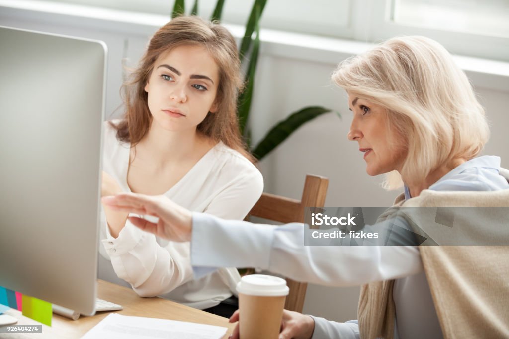 Senior and young colleagues discussing online project looking at screen Senior and young female colleagues discuss online project look at pc screen, older mentor teaches young woman explains corporate software work, aged executive helps intern, teamwork on computer task Trainee Stock Photo