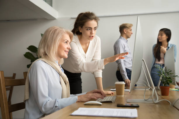 istock Young businesswoman teaching smiling senior colleague explaining computer applications work 926404294