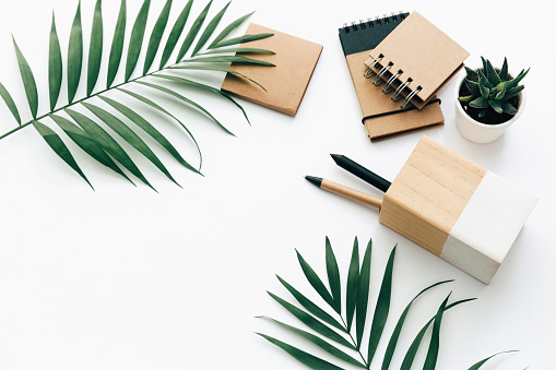 Minimal Office desk table with stationery set, supplies and palm leaves. Top view with copy space, creative flat lay.
