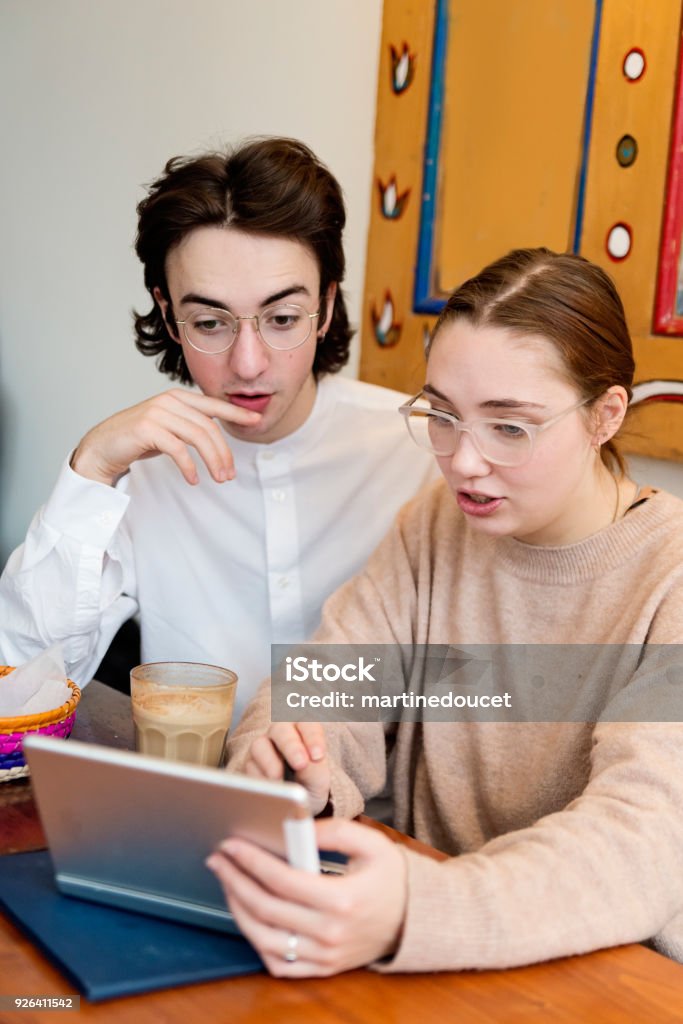 Young couple working on mobile tablet in a local coffee shop. Young couple in their twenties working on a mobile tablet in a local coffee shop. Vertical waist up indoors shot with copy space. This was shot in Montreal, Canada. 20-24 Years Stock Photo