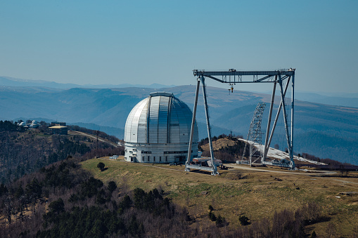 A special astrophysical observatory and a crane against the background of the blue sky and Caucasian mountains.
