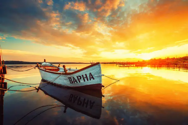 Photo of Fishing Boat on Varna lake with a reflection in the water at sunset.
