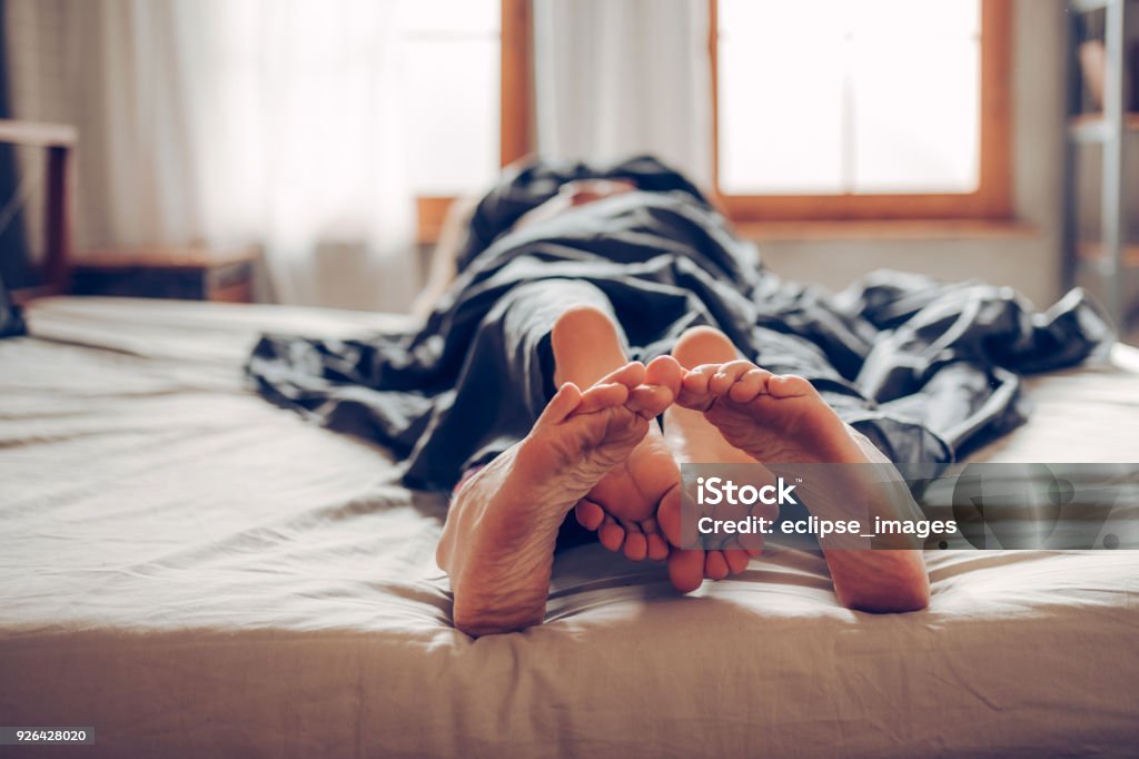 Our bed is short Adult couple's feet looking out of bed Sexual Issues Stock Photo