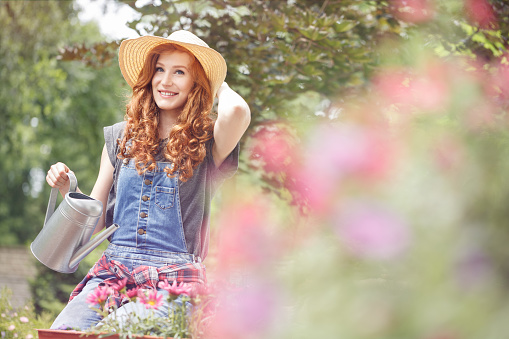 Beautiful woman in yellow sunhat relaxing in the backyard on a sunny summer day after gardening