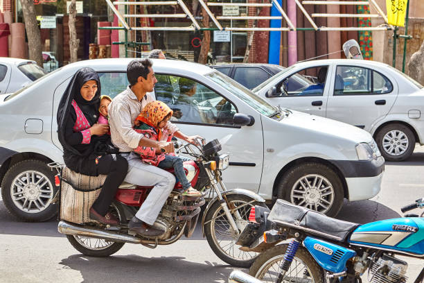 Kashan, Iran - April 27, 2017: A family of four, two little girls with their parents, ride a motorbike on a city street in traffic.
