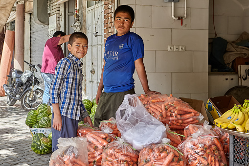 Kashan, Iran - April 27, 2017: Two teenagers are standing near sacks with fresh carrots in a vegetable shop.