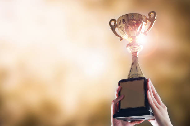 hands holding trophy cup on gold blurry bokeh background. - gold medal medal winning trophy imagens e fotografias de stock