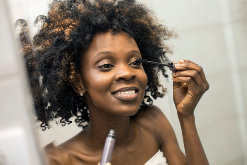 Young woman putting on mascara. About 25 years old, African female with curly hair.