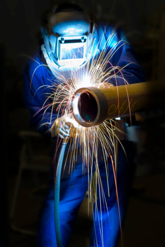 Closeup of Industrial welder with a torch and protective helmet welding metal profiles in factory