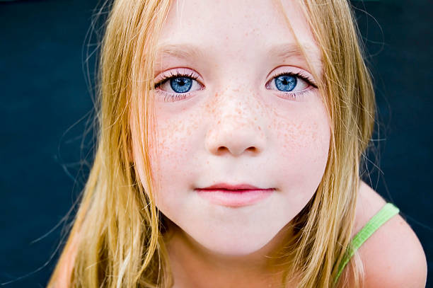 Close-up portrait showing eyes, nose and lips against a blurred backyard background. The image features selective focus on facial features with natural daylight. Garden furniture can be seen defocused in the background, suggesting an outdoor summer setting.