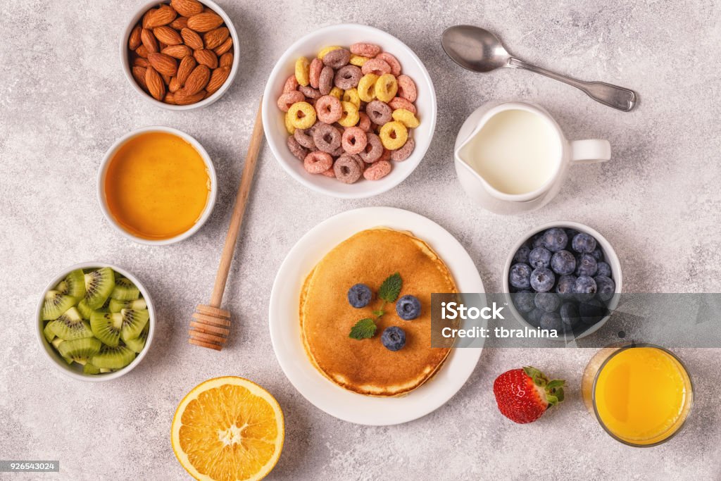 Breakfast with colorful cereal rings, pancakes, fruit, milk, juice. Breakfast with colorful cereal rings, pancakes, fruit, milk, juice. Top view. Backgrounds Stock Photo