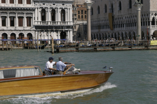 Venice, Veneto, Italy- June 26, 2023; On the grand canal of Venice-Italy, a couple of tourists take a ride on a gondola, typical maritime transport of Venice, the boat is steered by a man.