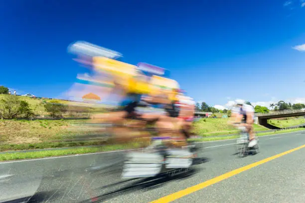 Cycling road race speed blur motion of tandem cyclists and individual unidentified closeup blue sky landscape.